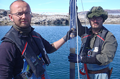 Nicolaj Larsen og Kurt Kjær ved Sydøstgrønland med en nyoptaget kerne. Man kan se overfladen af søens bund og overgangen til vandet. Foto: Anders Bjørk